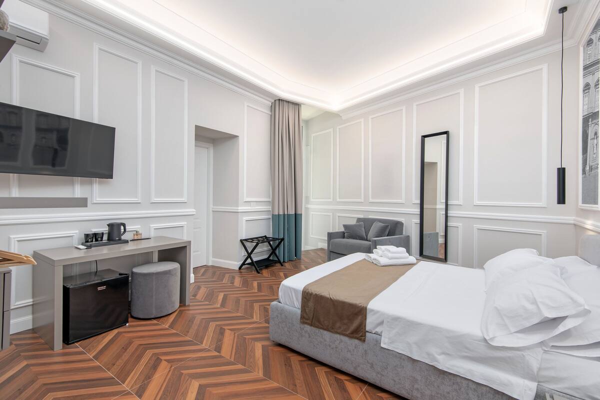 A modern hotel room with a bed, a desk, a television, and a seating area.