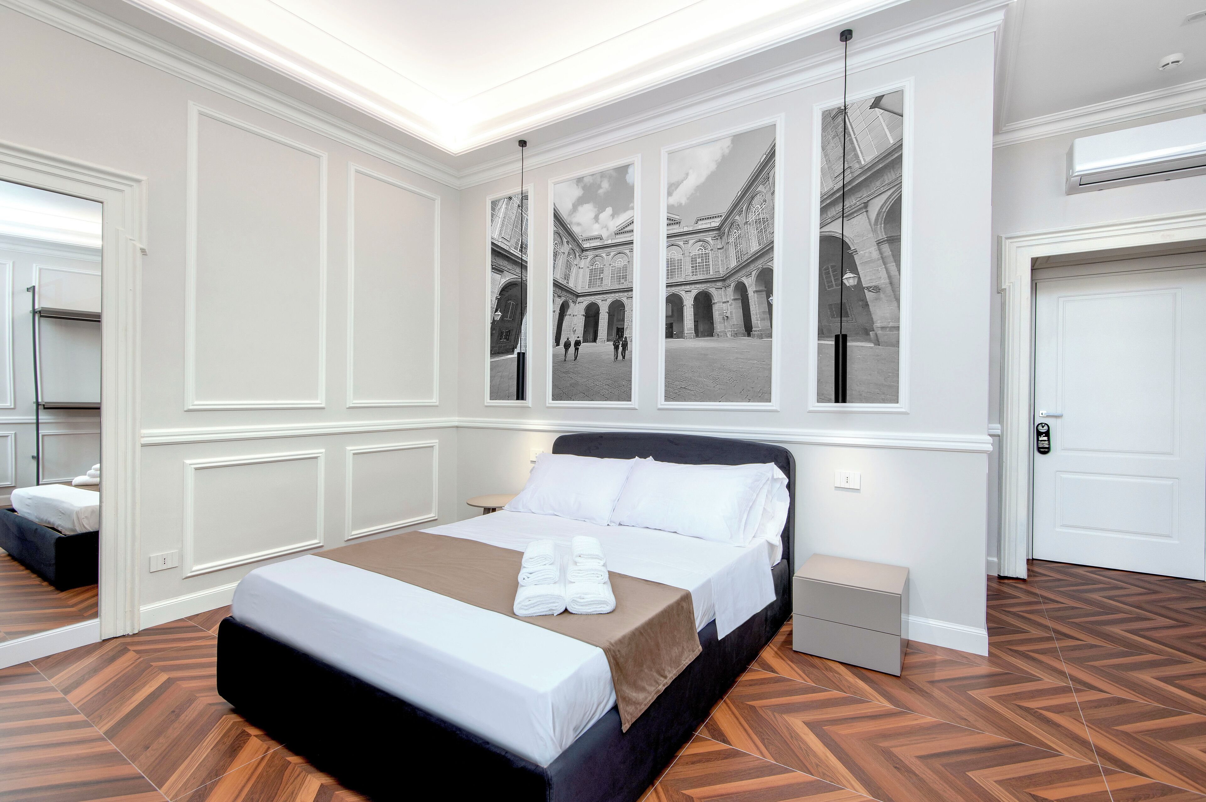 Una camera d'albergo con un letto grande, uno specchio, un armadio e un'opera d'arte appesa al muro raffigurante un edificio.