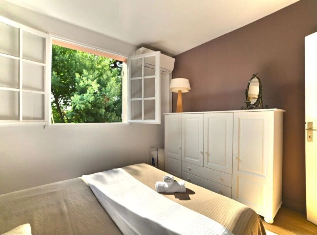 A bedroom with a bed, a window with a view of trees, a wardrobe, and a lamp.