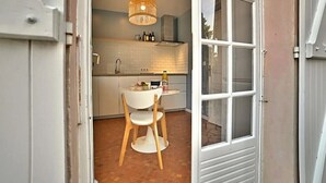 Una cocina con una mesa redonda y sillas, una lámpara colgante, y vistas a través de un ventanal.