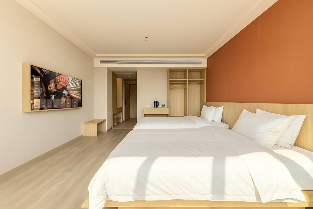 A hotel room with a large bed, a wardrobe, a bedside table with a lamp, and a painting on the wall.