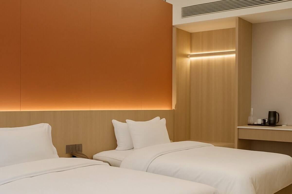 A hotel room with two beds, a wooden headboard, a nightstand, and a small table with a coffee maker.