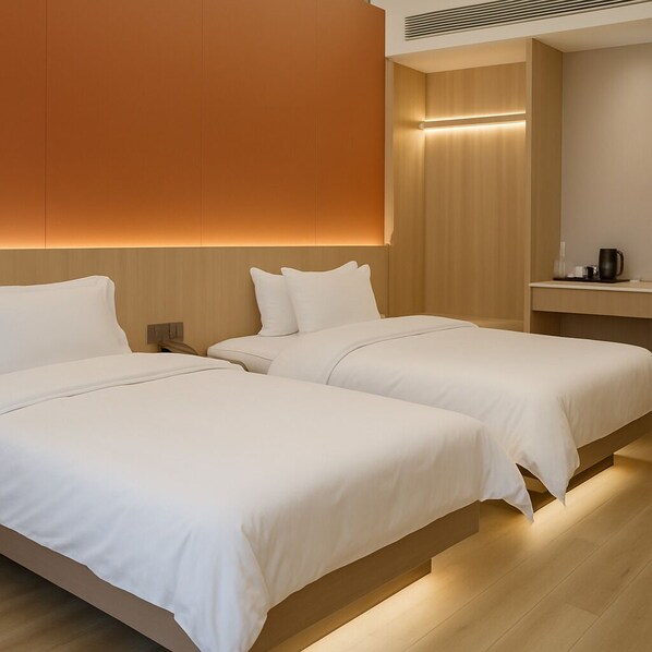 Quarto de hotel com duas camas, uma cabeceira de madeira, uma mesinha de cabeceira e uma pequena mesa com cafeteira.