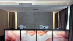 A reception desk with a modern design, featuring a marble-like wall and a large floral print. There are two laptops on the desk, and a small sign with a QR code. - Crystal Hotel (Bishkek)