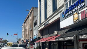 Vista de la calle con un edificio que muestra la señalización de "Ais Sigorta" y "Hamur Kovani Pasta & Cafe Restaurant".