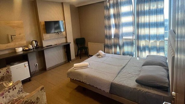 Una habitación de hotel moderna con cama, escritorio, silla, televisor y ventana con cortinas.
