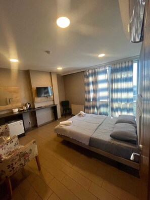 A modern hotel room with a bed, a desk, a chair, a TV, and a window with curtains. - Joi Suite Hotel (İstanbul)