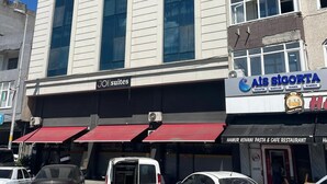 Un edificio con un letrero que indica 'JOI suites' y 'Ais Sigorta' en la planta baja. Hay coches estacionados adelante.