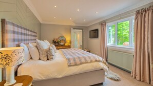 Ein Schlafzimmer mit Bett, Nachttisch, Lampe und einem Fenster mit Vorhängen.