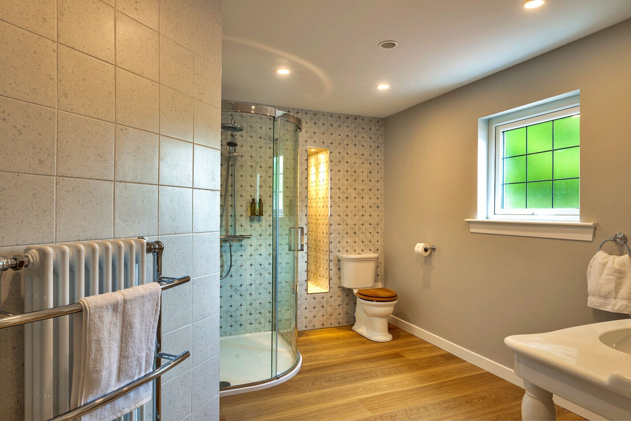 Un baño con cabina de ducha de vidrio, inodoro, lavamanos y ventana con vidrio tintado de verde.