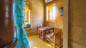 Quarto com uma mesa e cadeiras de madeira, uma janela com cortinas e um detalhe decorativo na parede.
