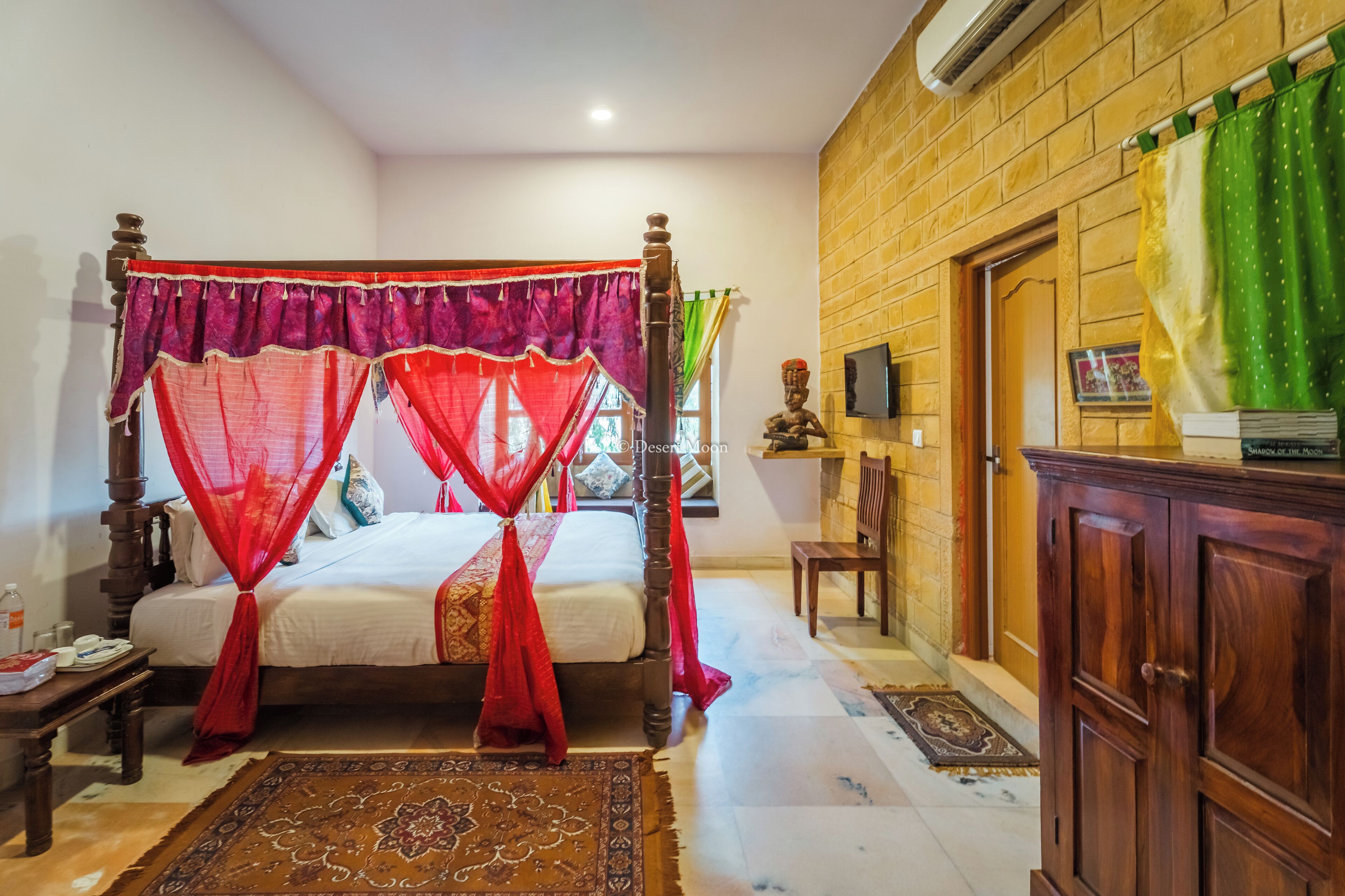 A traditional four-poster bed with red canopy, a wooden nightstand, a green curtain, and a brick wall.