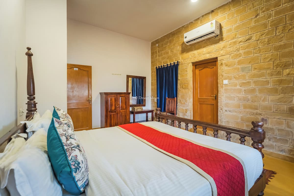 A bedroom with a large bed, wooden headboard, a red and white bedspread, a wooden dresser, and a stone wall.