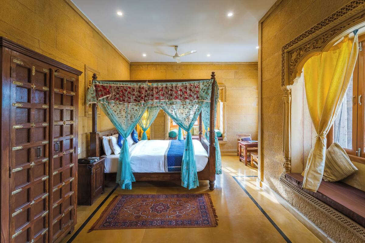 A spacious bedroom with a four-poster bed, a wooden wardrobe, and a large window with curtains.