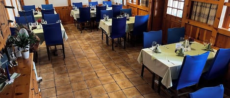 Um restaurante com várias mesas e cadeiras azuis, paredes de madeira e chão ladrilhado.