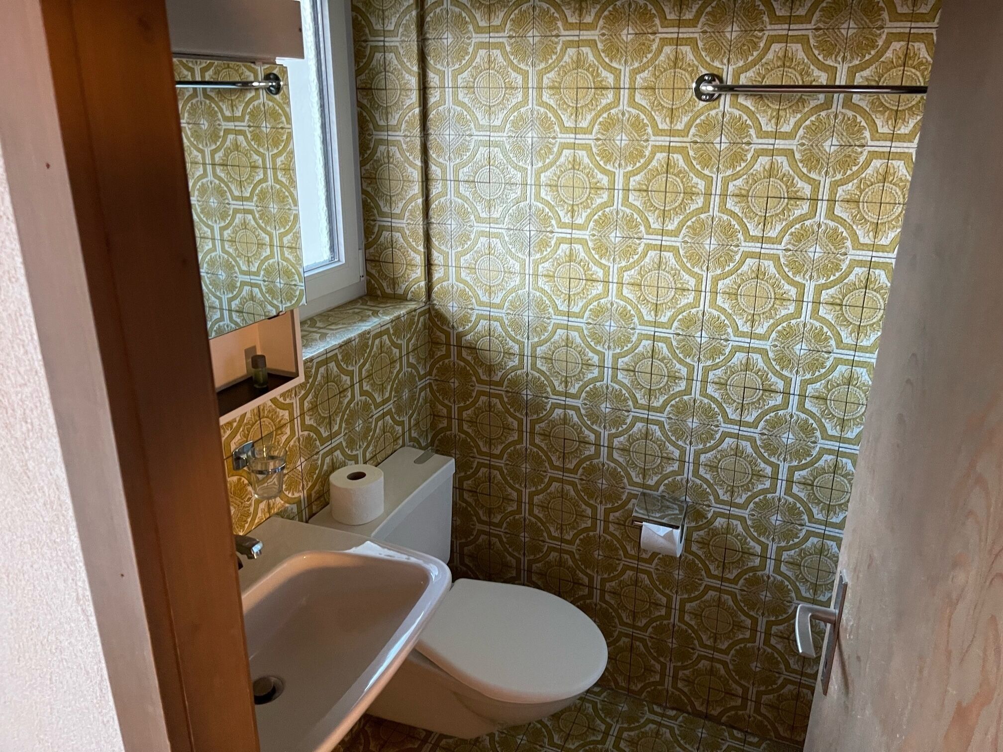 Un baño con inodoro, lavamanos y una ventana sobre el lavamanos.