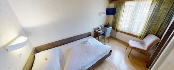 A hotel room with a bed, desk, chair, and a television on the wall.