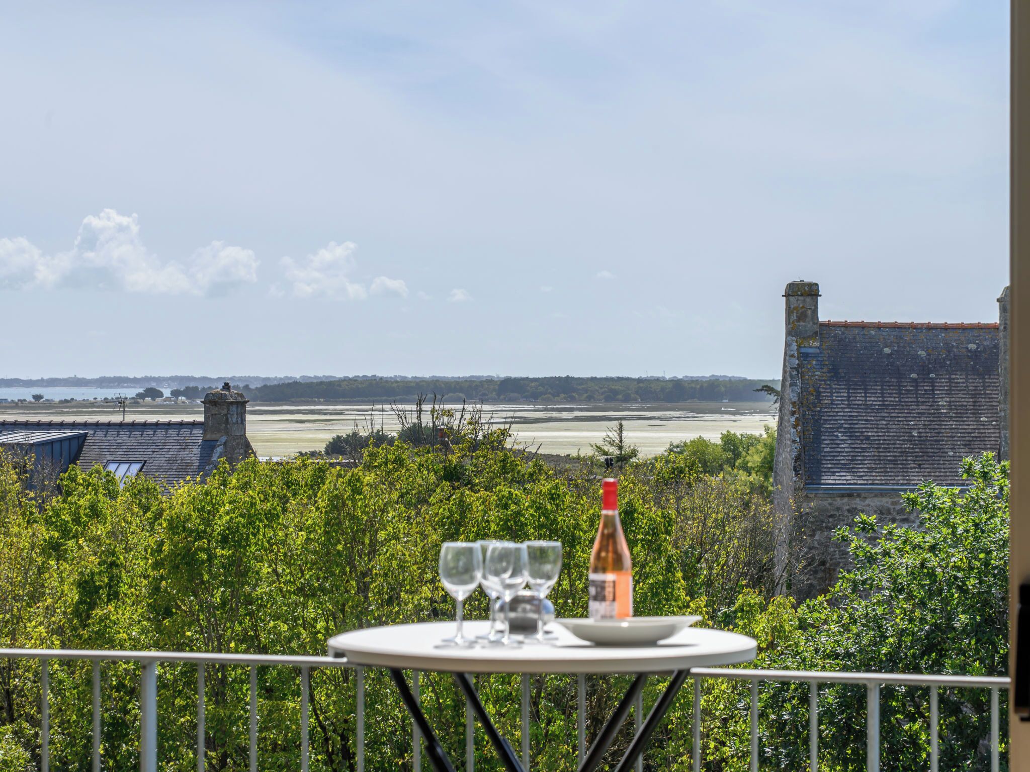 Ein Tisch mit Weingläsern und einer Flasche, vor einer Kulisse aus üppigem Grün und einer entfernten Küstenlandschaft.