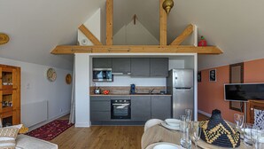 A compact kitchen with modern appliances, a dining area with a wooden table set for four, and a cozy living space with a sofa and decorative pillows.