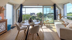 A dining area with a table set for four, surrounded by chairs, with a view of greenery and a building in the background.