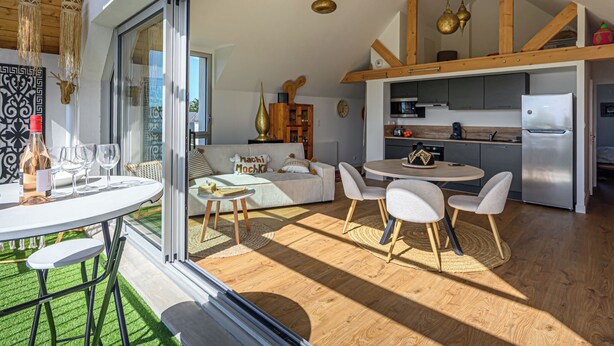 A modern kitchen with a built-in oven and refrigerator, a dining area with a round table and chairs, and a cozy seating area with a sofa and cushions.