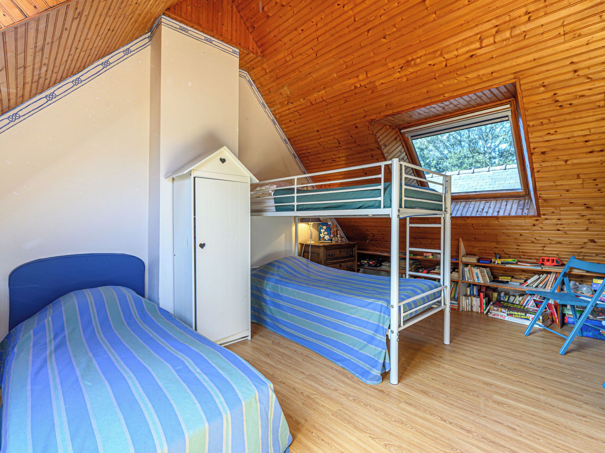 Un dormitorio acogedor en el ático con literas, un armario y una ventana con vistas a la vegetación.