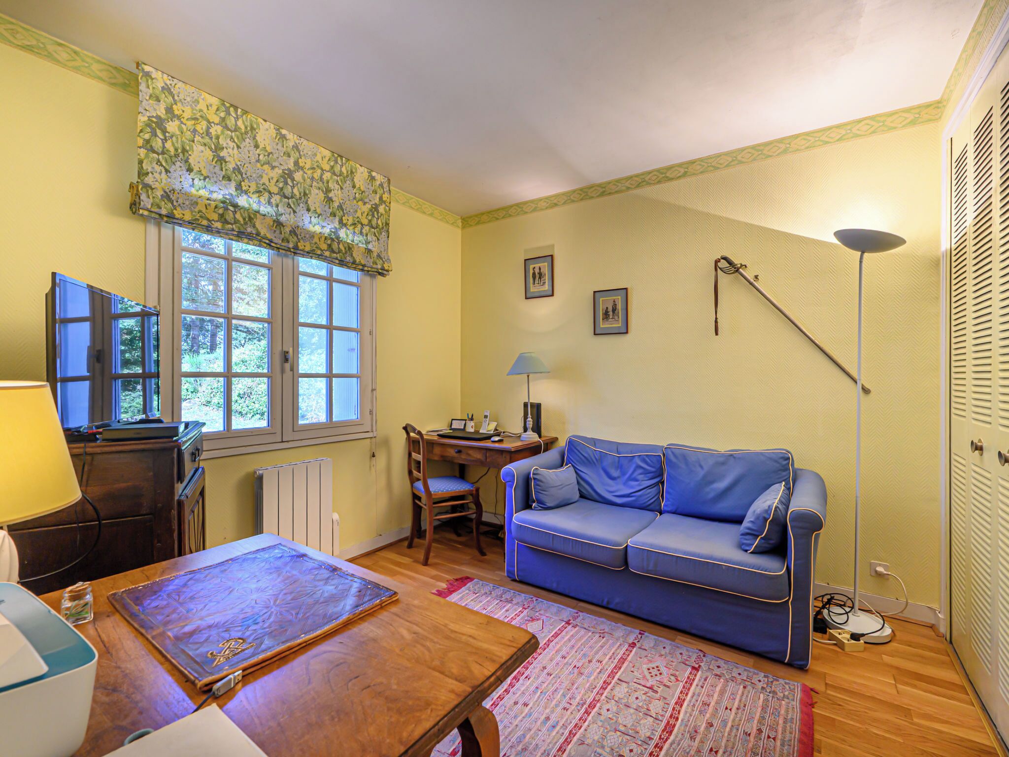 A cozy living room with a blue sofa, wooden coffee table, and a desk with a lamp.