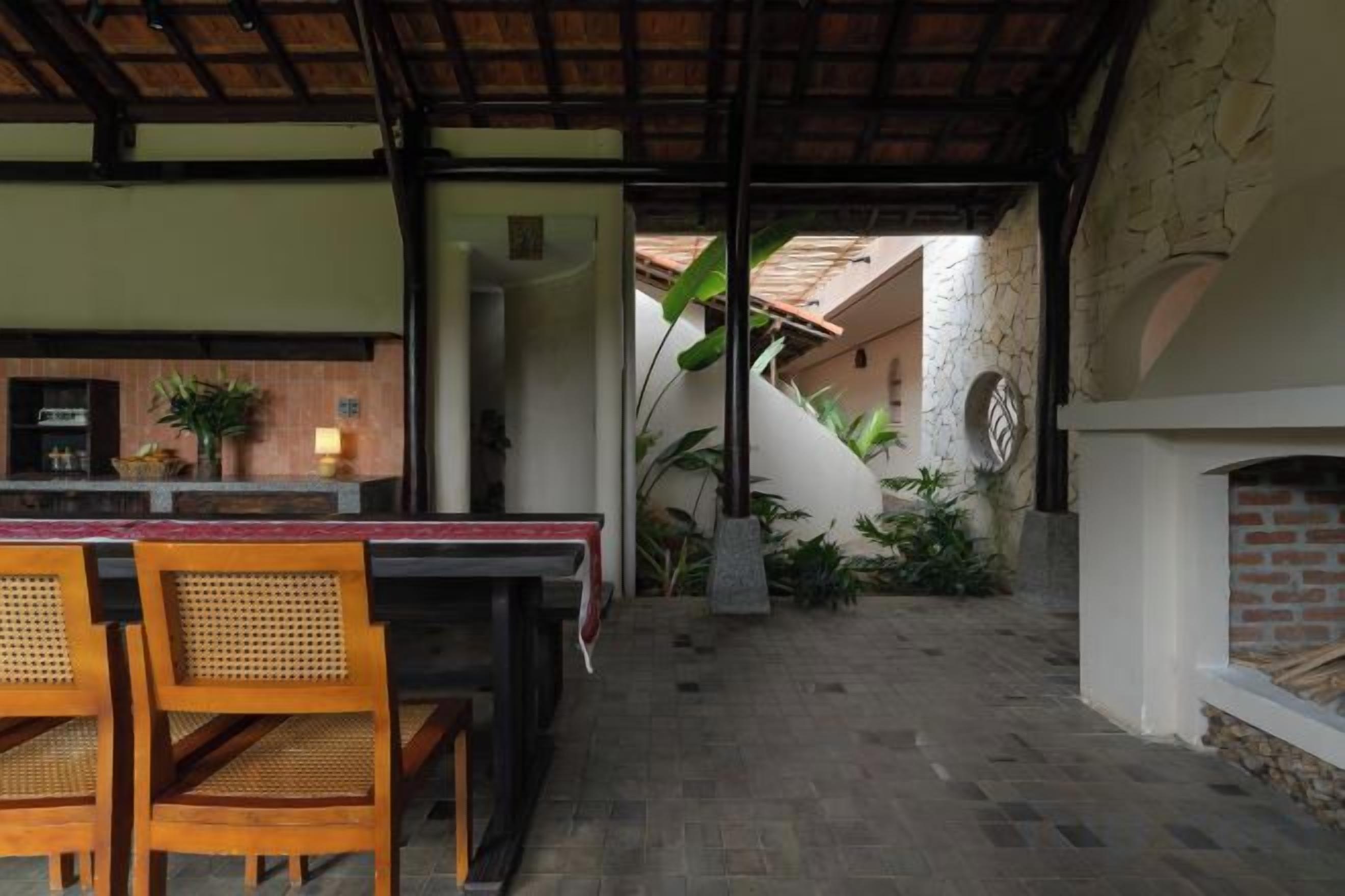 Un espacio de comedor al aire libre con una mesa, sillas, una chimenea de ladrillo y una escalera que lleva a un nivel superior.