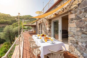 A dining area with a table set for breakfast, stone walls, and a view of the surrounding landscape. - Relais Le Torri in Verici (Casarza Ligure)