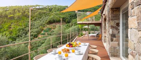A terrace with a table set for breakfast, overlooking a lush landscape.