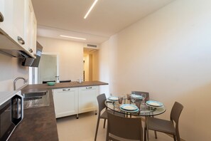 A compact kitchen with white cabinets, a stainless steel range hood, and a glass dining table set with plates and glasses. - Relais Le Torri in Verici (Casarza Ligure)