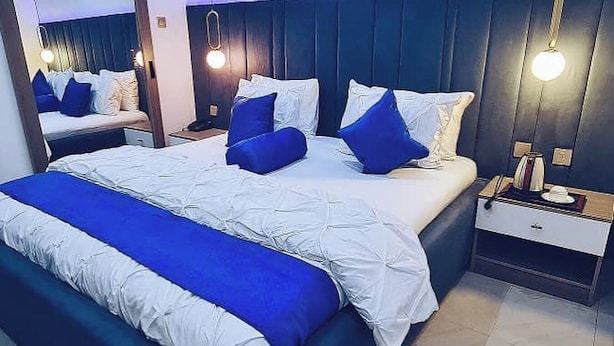 A modern bedroom with a large bed, a nightstand, a mirror, and a ceiling light fixture. - The Oak Residence (Abuja)