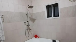 A bathroom with a white bathtub, a showerhead, and a small window. - The Oak Residence (Abuja)