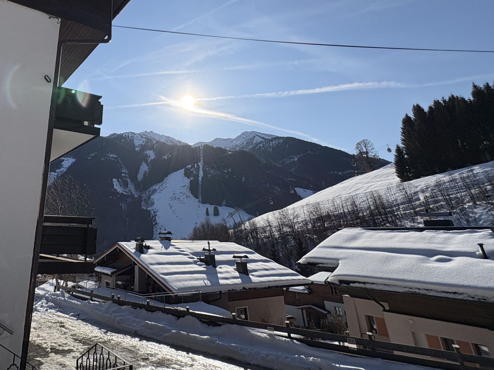 A mountain view with a ski lift, snow-covered roofs, and a clear sky.