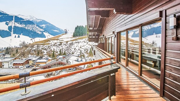 Un balcon en bois offrant une vue sur un paysage montagneux enneigé.