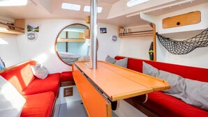 A compact interior with a bunk bed, a small table, and a hammock. - Sailing Boat 'Voilier Pyman - Le Chant Des Voiles' with Sea View and Private Terrace (Douarnenez)