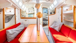 A compact interior with a central table, red seating, and a netted hammock. - Sailing Boat 'Voilier Pyman - Le Chant Des Voiles' with Sea View and Private Terrace (Douarnenez)
