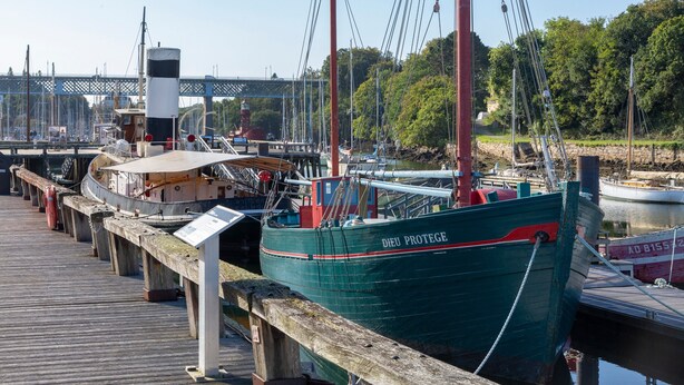 A dock with boats, a wooden walkway, and a bridge in the background. - Sailing Boat 'Voilier Pyman - Le Chant Des Voiles' with Sea View and Private Terrace (Douarnenez)