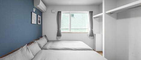 A bedroom with two beds, a window with curtains, a wardrobe, and a wall-mounted air conditioner.