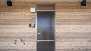 A metallic door with a keyhole and a handle, set in a brick wall with a small utility box and a water meter to the left. - CHARMANT 1A (Minamifurano)