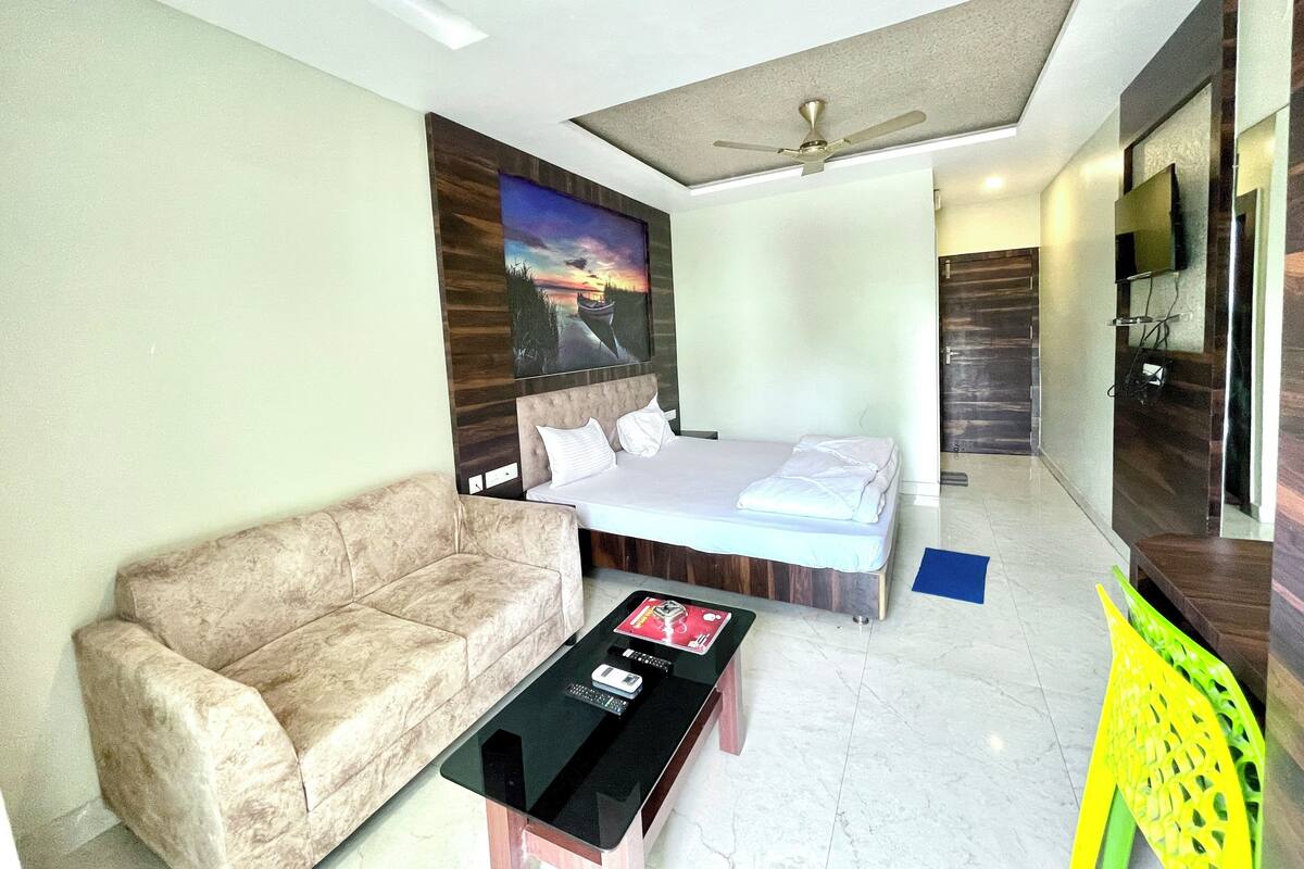 A modern hotel room with a bed, a sofa, a coffee table, a ceiling fan, and a painting on the wall.