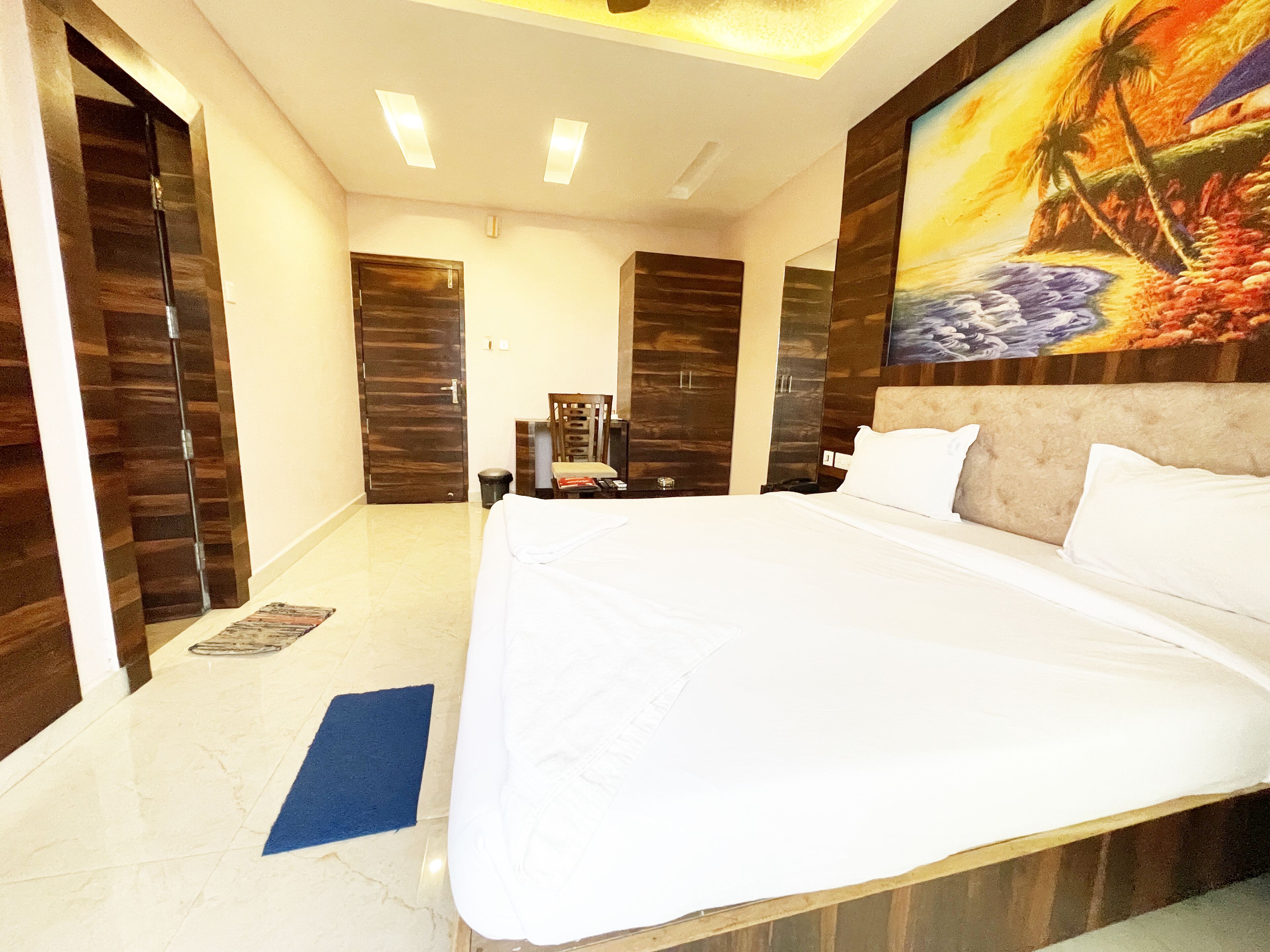 Une chambre d’hôtel avec un grand lit, une armoire en bois et un tableau représentant une scène de plage.