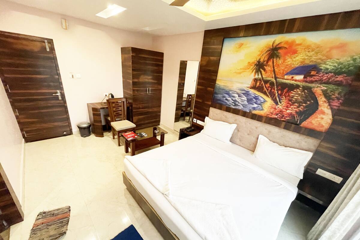 A hotel room with a large bed, a desk, a chair, a wardrobe, and a painting on the wall.
