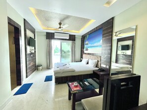 A hotel room with a bed, a desk, a chair, a TV, and a ceiling fan. - Hotel Rohit Rohini (Puri)