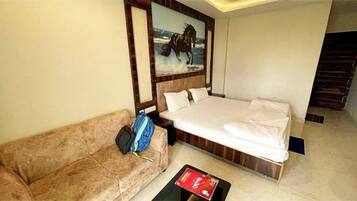 Una habitación de hotel con cama, sofá, un cuadro y una mesa de centro.