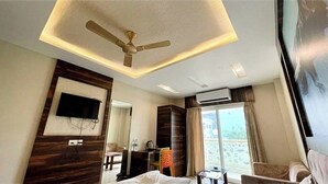 Una camera d'albergo con ventilatore a soffitto, TV a schermo piatto fissata al muro, un letto, una scrivania e una sedia.
