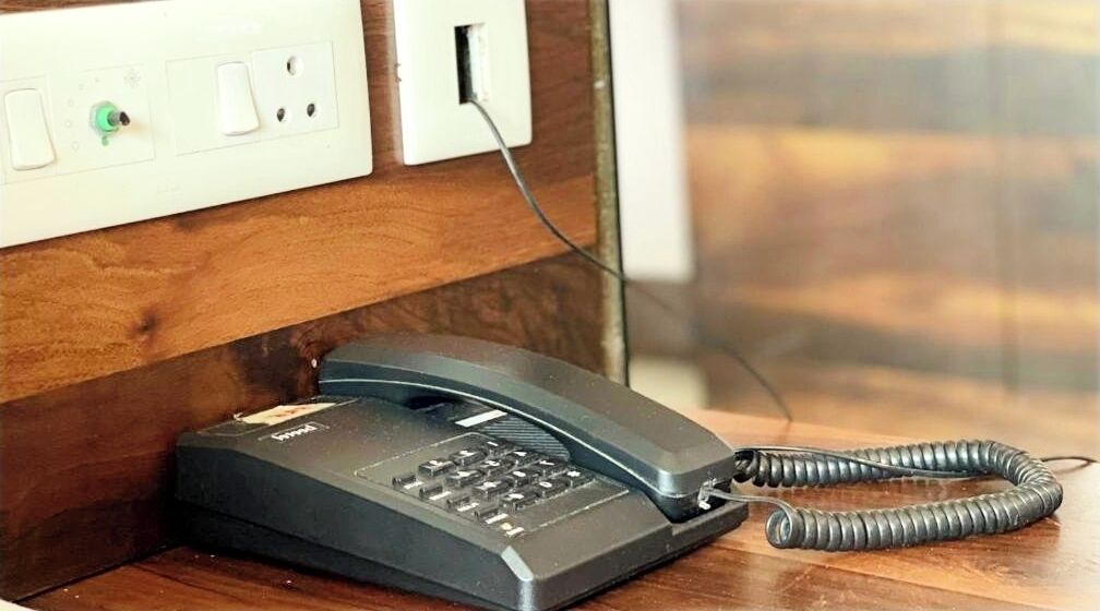 Un teléfono sobre una superficie de madera con un cable enrollado, conectado a un enchufe de pared.