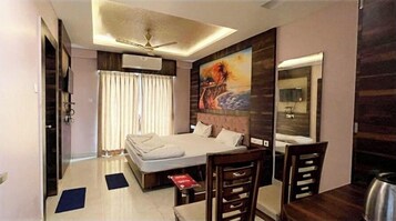 Une chambre d’hôtel avec un lit, un bureau, une chaise, un ventilateur de plafond et un grand tableau accroché au mur.