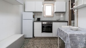 A compact kitchen with white cabinets, a built-in oven, a window above the sink, and a table with a patterned tablecloth. - Casina del Parco by Wonderful Italy (Bari)