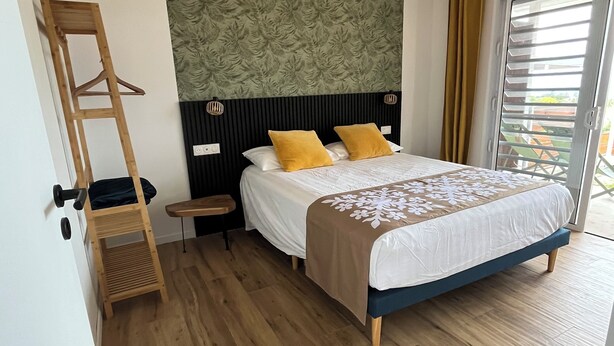 A bedroom with a bed, a wooden ladder, a small table, and a window with blinds. - A modern, well-equipped bungalow with an exceptional view of the lagoon! (Bora-Bora)